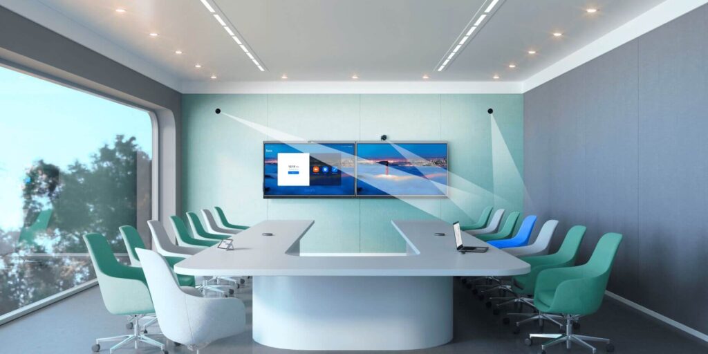 A meeting room with a television screen hung on the wall and chairs surrounding a U-shaped table