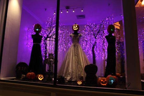 Halloween store display with mannequins, jack-o'-lanterns, and purple lights.