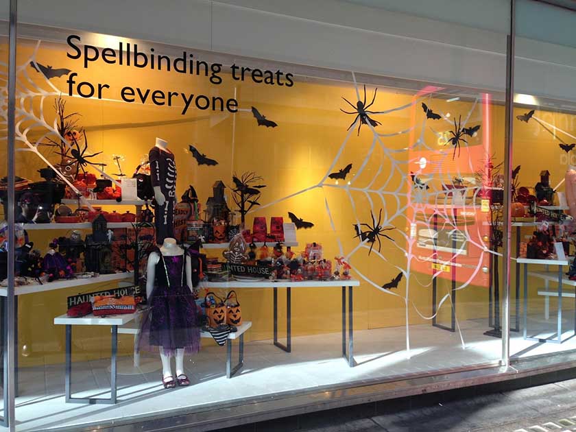 Halloween window store display featuring bats, spider webs, and haunted house decorations.