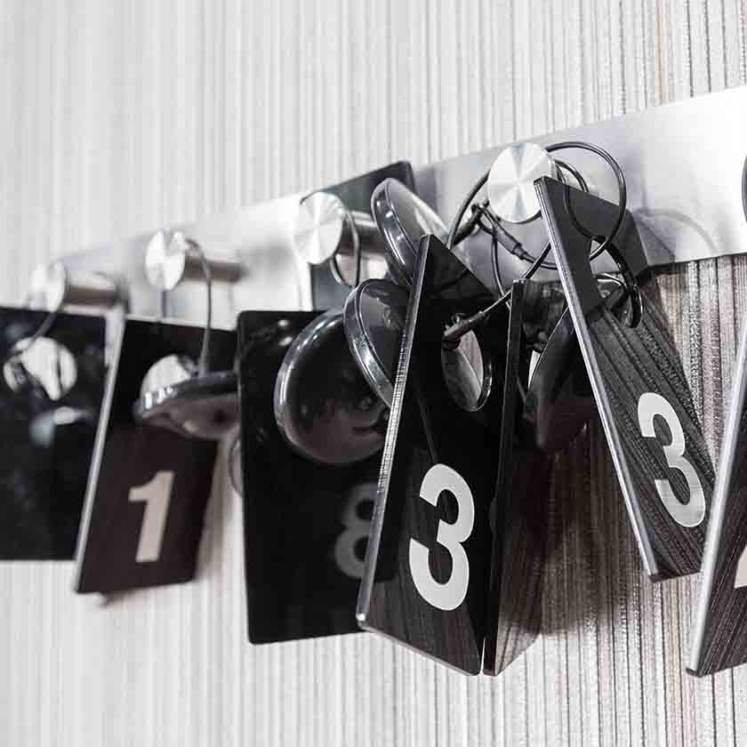 Six black tags with numbers various printed numbers hanging on metal hooks.