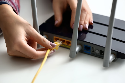Woman inserting ethernet wire into wi-fi router on white table, closeup