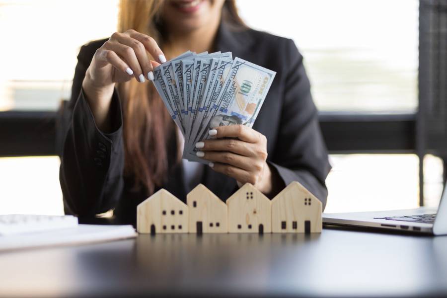 a professional woman counting money above a wooden cutout of houses.
