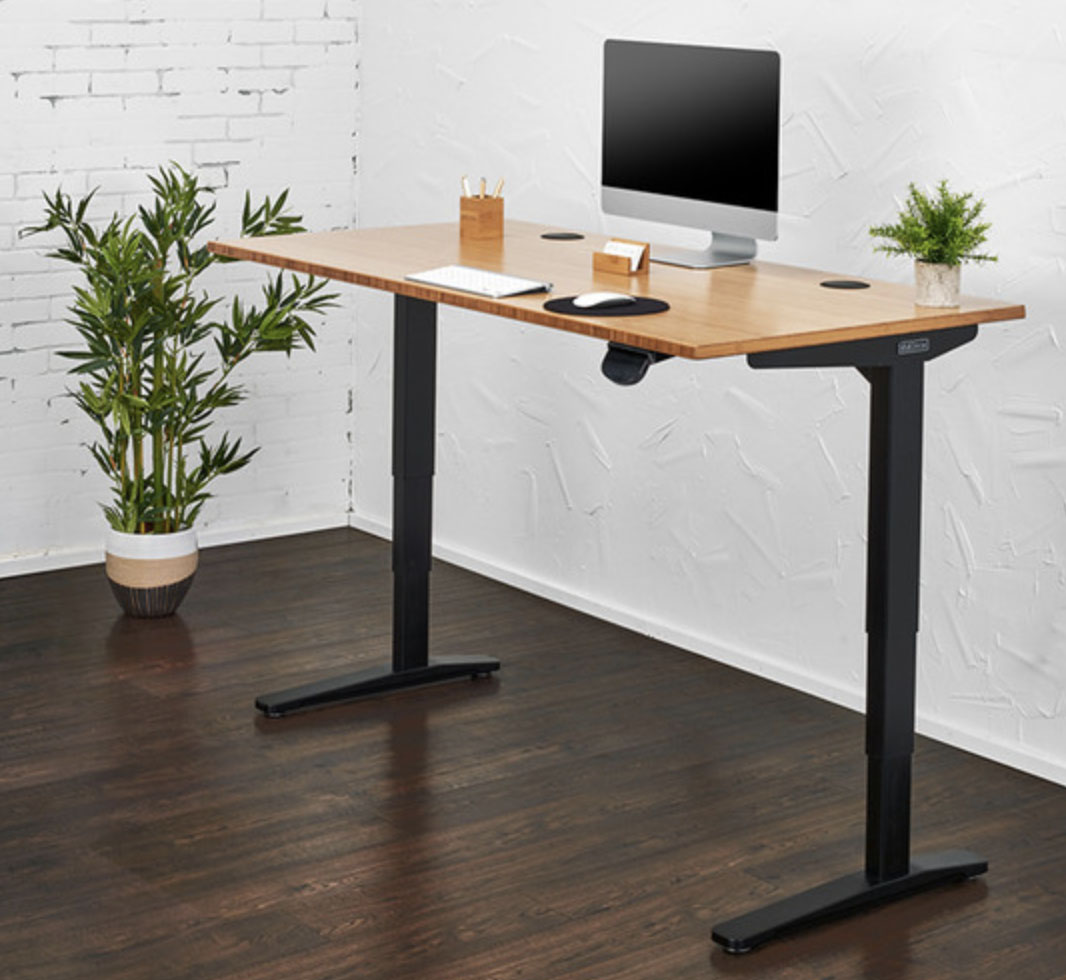 UPLIFT Standing Desk with a monitor, keyboard, and office supplies placed on top.
