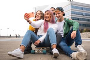 Group of four teens in a skatepark taking a selfie on a smartphone in an orange case.