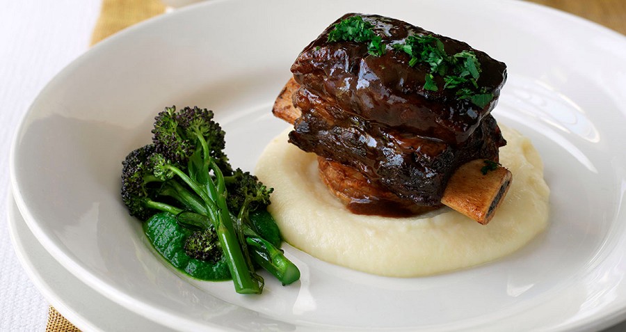 Braised short rib on top of mashed potatoes with a side of broccoli on a plate