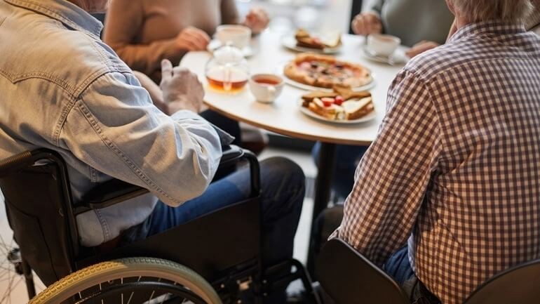 Group of people, including one person in a wheelchair, dining over an appropriate-height dining surface.