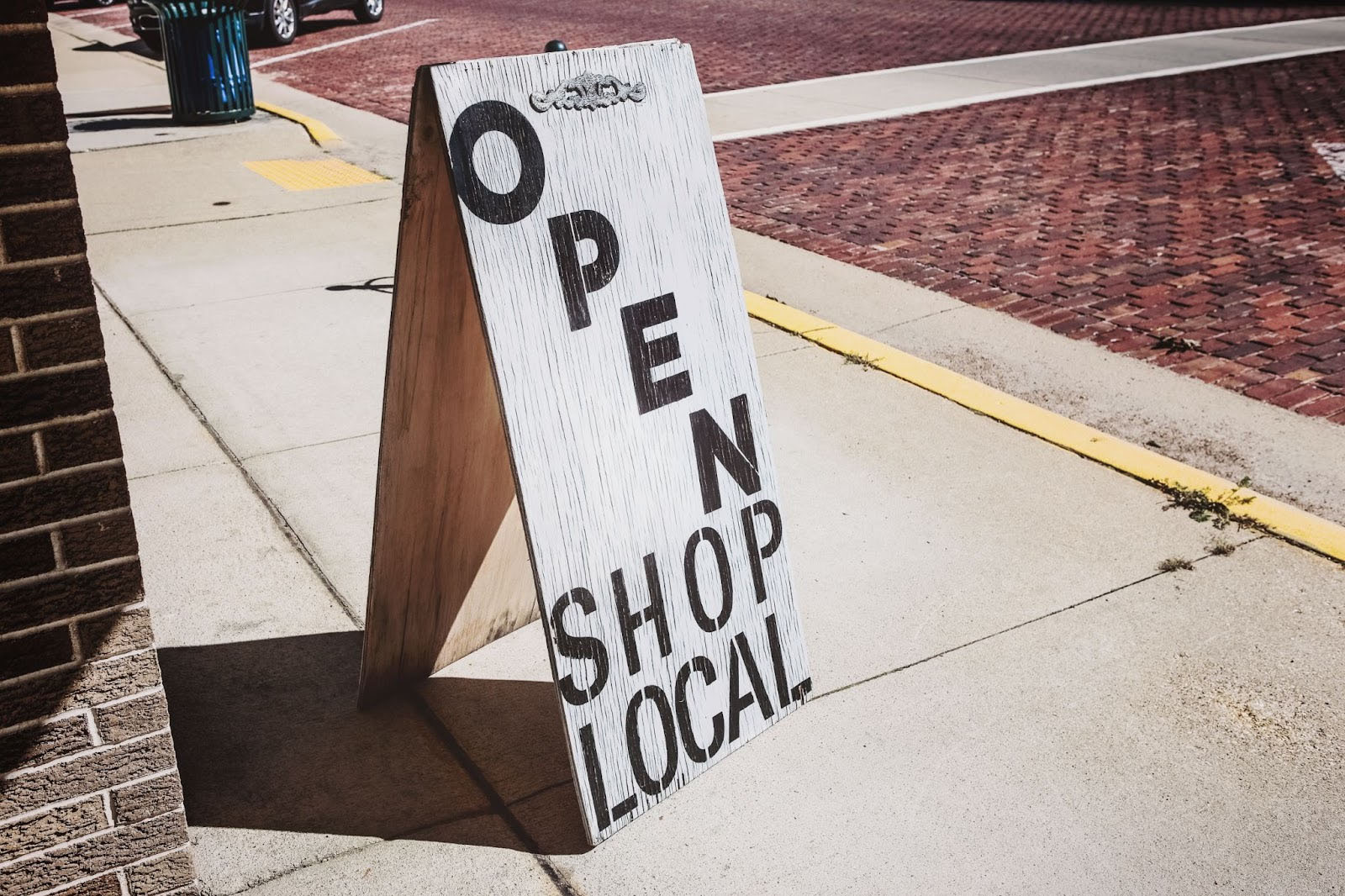 A sandwich board that reads "OPEN SHOP LOCAL" set up on a sidewalk next to a building.