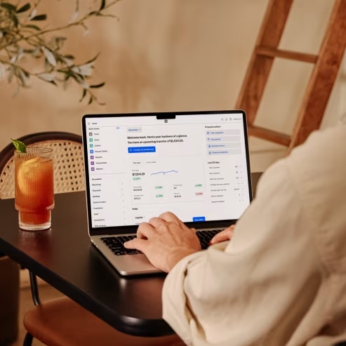 Person sitting at a table using a computer with a drink next to it.