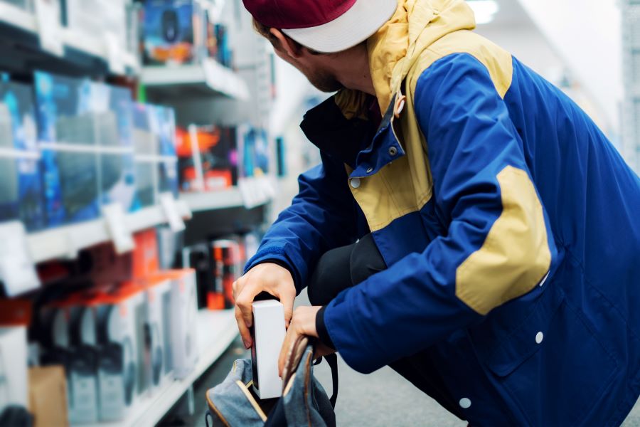 Consumer hands are shown in close-up, placing the newly acquired gadget into their pocket while in the store.