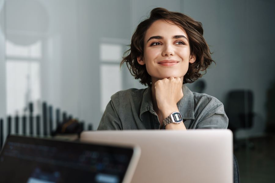 Image of young joyful woman smiling while working with laptop