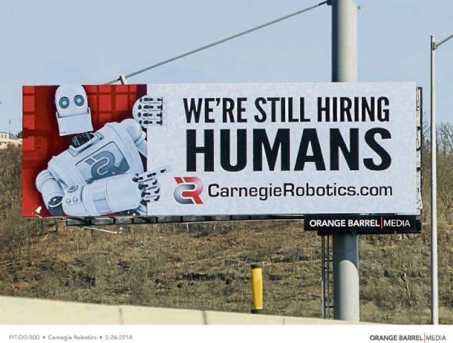 Carnegie Robotics billboard Now Hiring sign featuring a robot and the caption "still hiring humans"