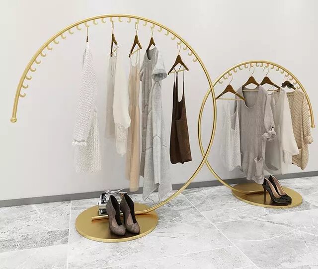 Curved gold clothing racks with neutral colored clothes hanging from them