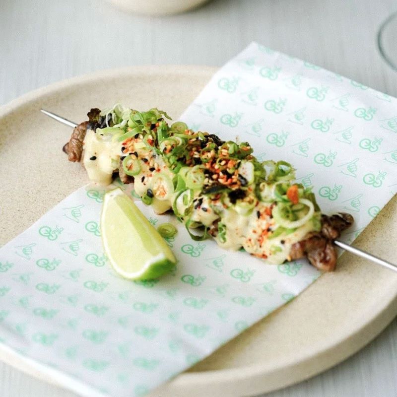 A skewer of food and a lime resting on a paper-lined plate