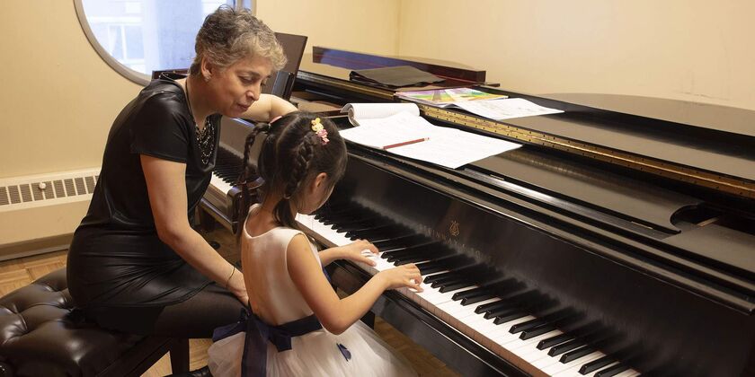A person sitting at a piano next to a young child who has her hands positioned on the keys.