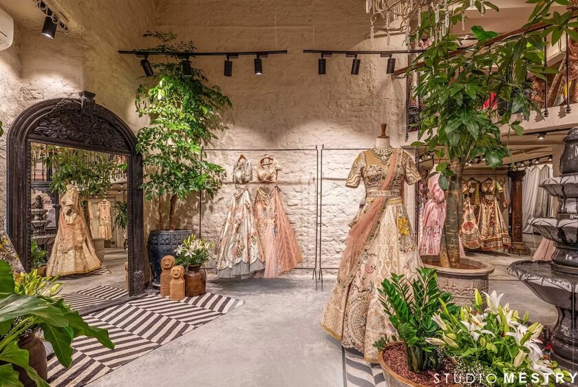 Store selling Indian women's formal wear with lots of greenery, mannequins, and a large mirror