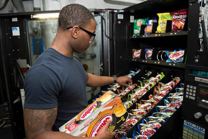 A person loading bagged snacks into an open vending machine.