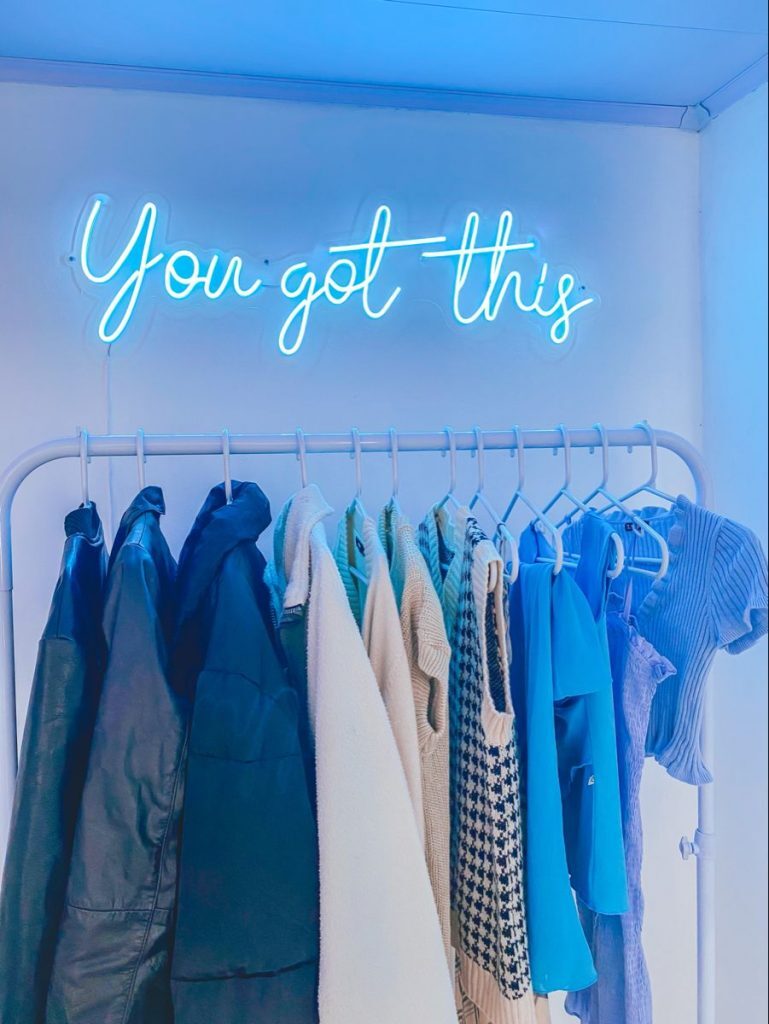 'You Got This' blue neon sign above clothing rack