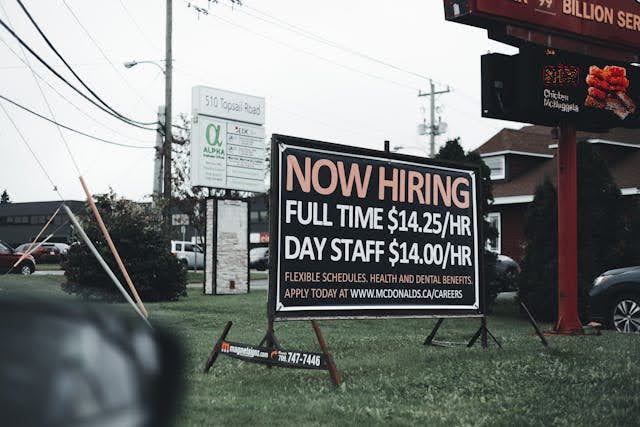 A large hiring sign that displays wage, schedule, benefits, and how to apply