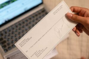 Person holding a cheque in front of a laptop