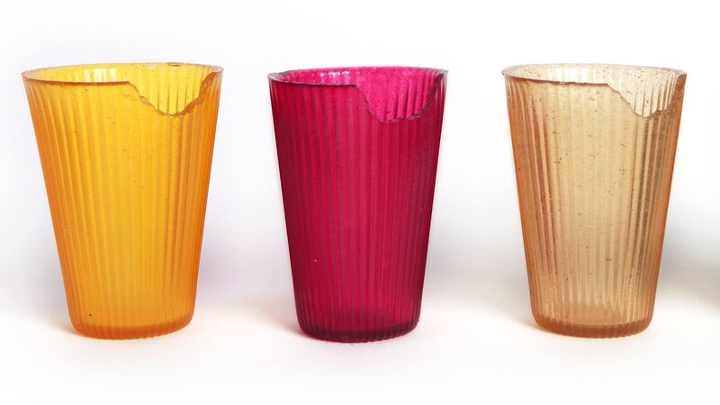 Three drinking cups made of translucent, colorful material with bites taken out of each rim.