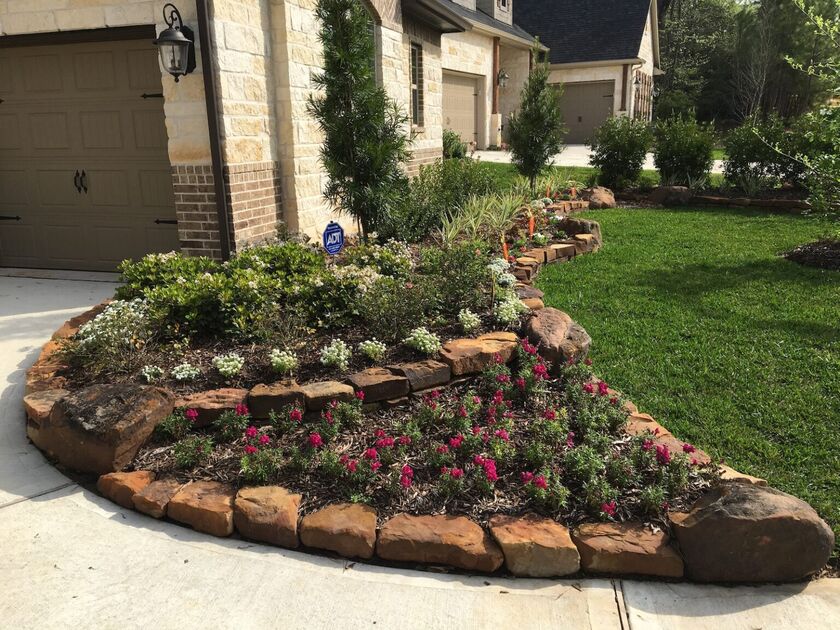 a front yard with a garden composed of flowers within a border make of red boulders.