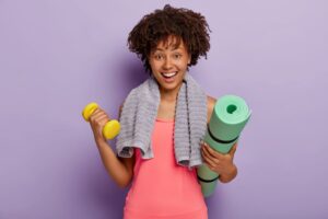 A woman equipped with a fitness mat and a dumbbell, prepared to start her workout session.