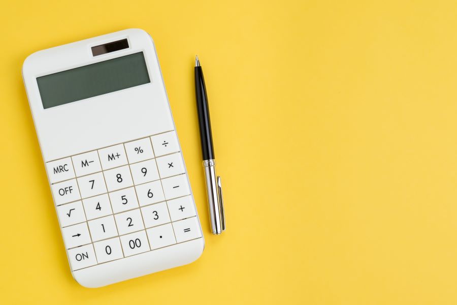 white calculator with pen on solid yellow background. Cost calculation concept.