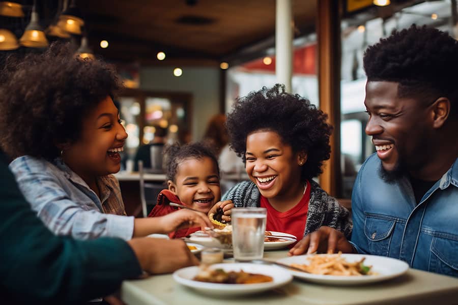 African-American family having fun spending time eating meal at outdoor restaurant.