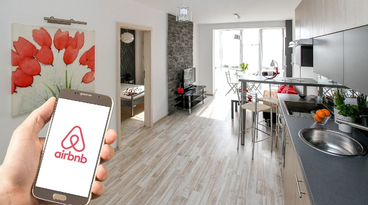 Man in small apartment holding a smartphone with AirBnB app