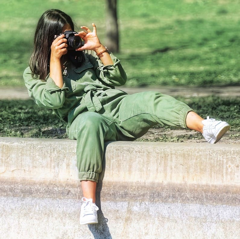 Woman in green sitting on the grass taking a photo with a professional camera