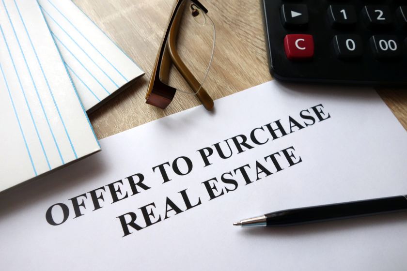 Document showing an offer to purchase real estate with pen, calculator, and glasses on a desk.