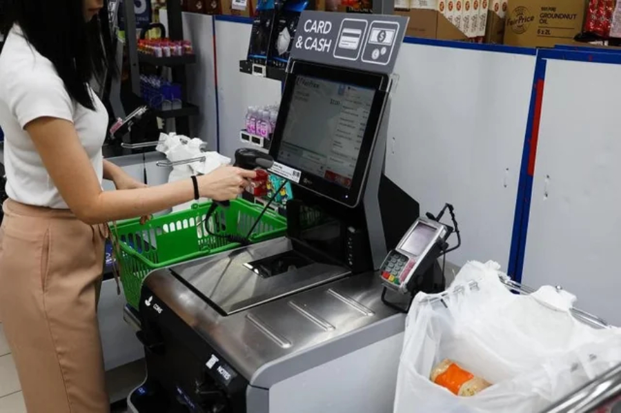 A woman using the self-service payment counter in a grocery store.