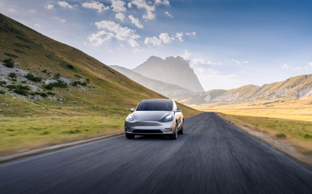 Tesla Model Y driving down an empty road in open countryside with mountain in background