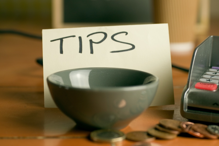 Closeup shot of a bowl near a contactless pdq machine and a tips note leaning on a coffee cup.