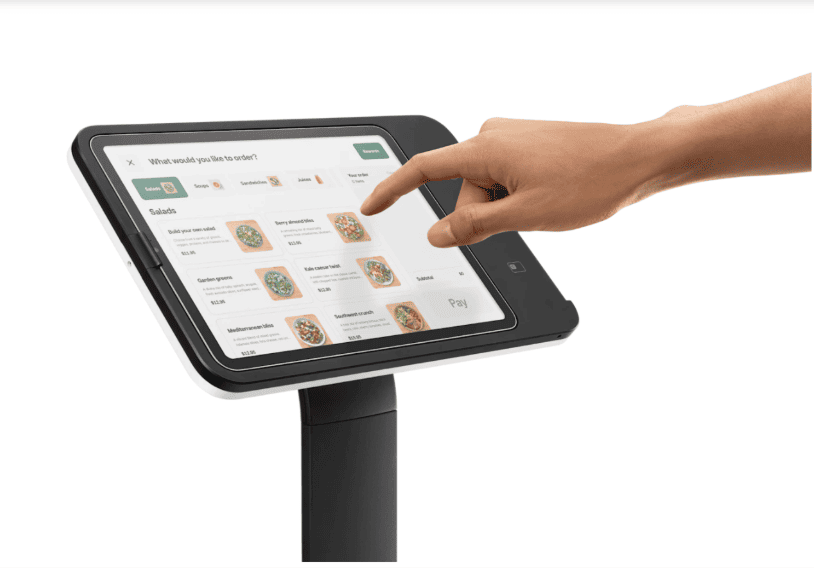 Customer using a Square self-service kiosk with touchscreen menu for restaurant ordering.