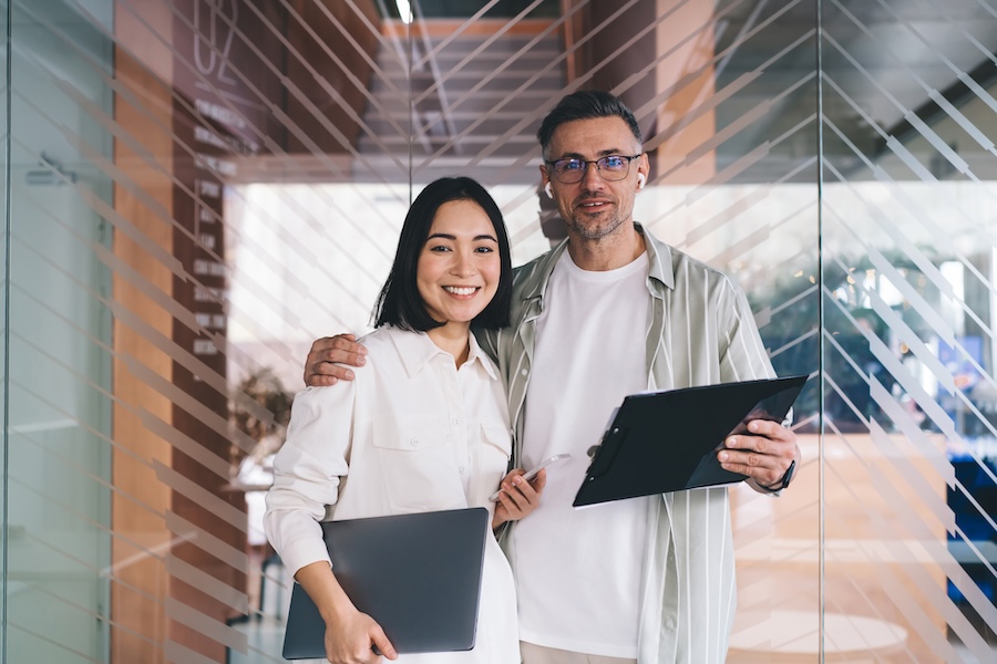 Cheerful diverse business partners standing near glass door