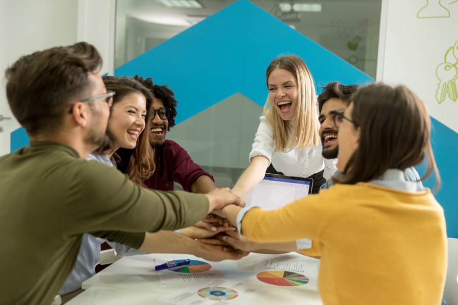 Team of young people stacking hands together over table engaged in teambuilding.