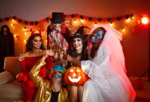 Group of cheerful friends in spooky halloween costumes posing with glasses of champagne in hands.