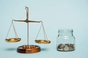 Bronze justice scales balanced near a glass jar filled with coins on a blue background, symbolizing anti-corruption and fairness in financial practices.