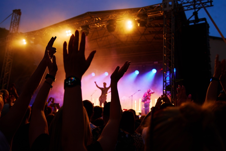 Crowd at a music festival at night with hands in the air foreground with the lead guitarist of a band waving to the crowd.