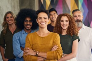 A diverse group of six confident people standing together, smiling, with a colorful geometric background.