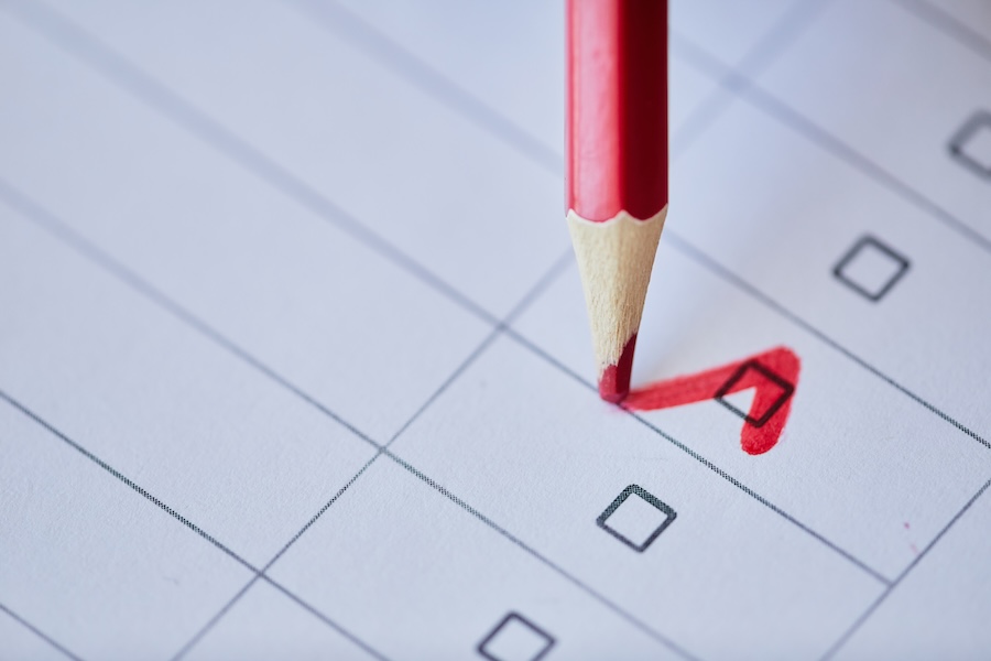 A red pencil writing a checkmark inside a check box.