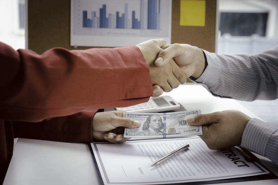 Businessman and businesswoman making handshake with money in hands