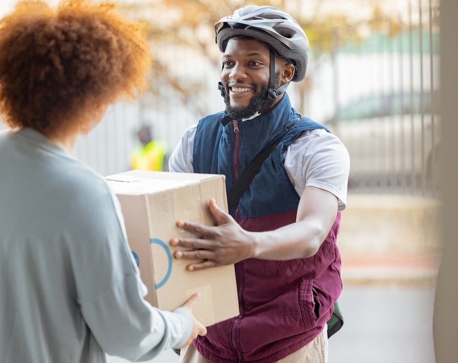 Delivery person handing a cardboard box to a woman at her doorstep.