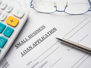 Business loan application form on desk with eyeglasses and calculator.