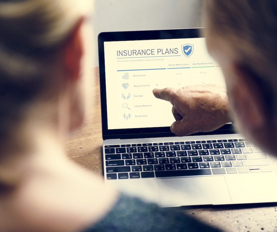 Two individuals reviewing insurance plans on a laptop screen, with one pointing at the details displayed.