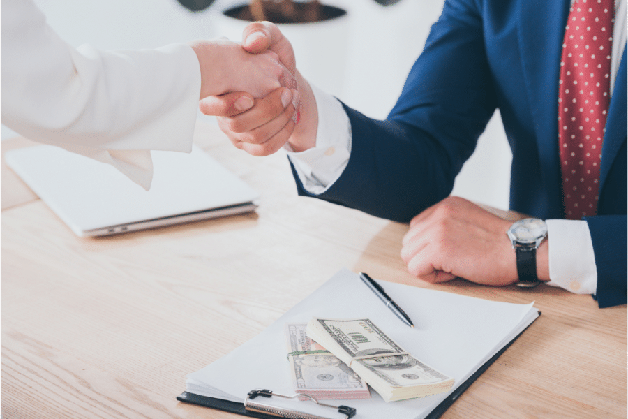 woman shaking hands with businessman near dollar banknotes on table