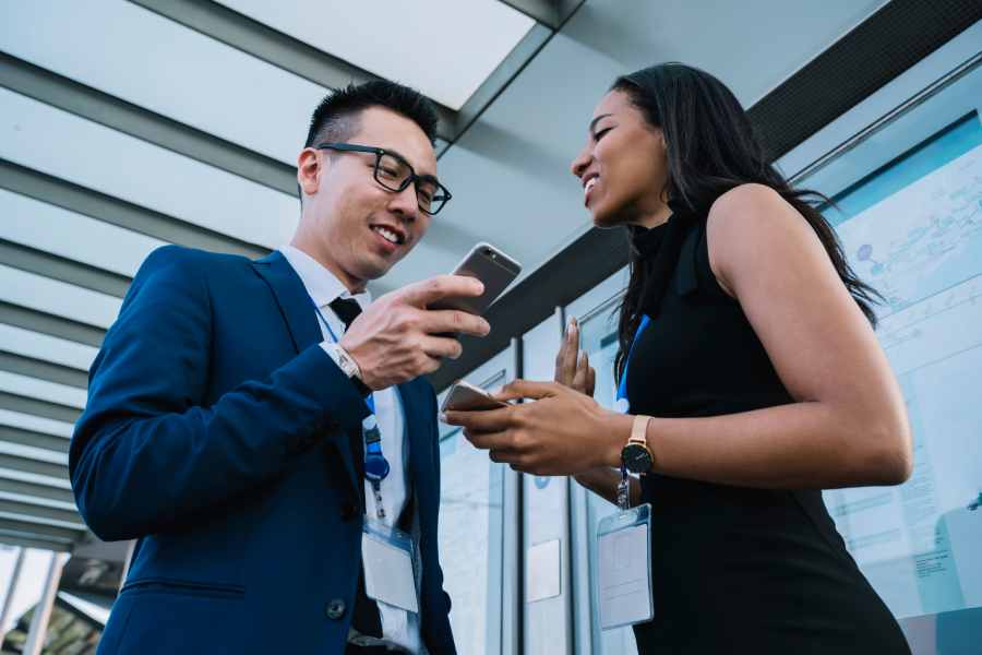 Employee standing next to colleague and communicating while using cellphone.