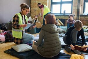 Female volunteer with mobile gadgets sitting on squats in front of refugee.