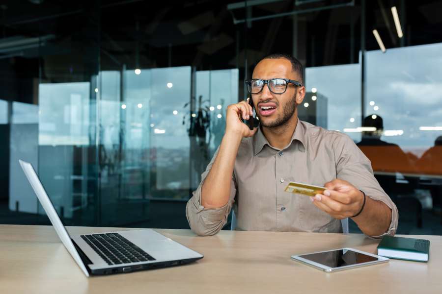 Dissatisfied businessman in the office with a bank credit card calls customer support.